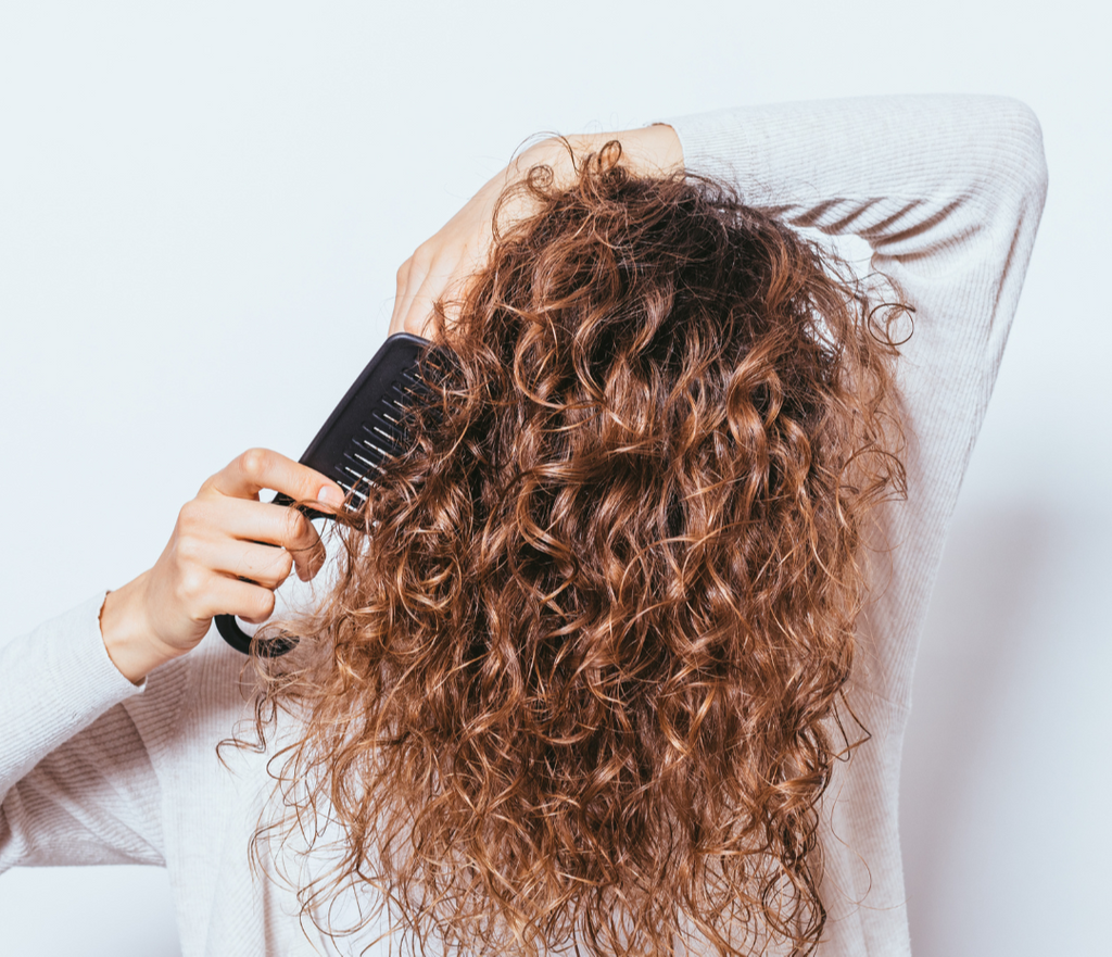 Person with curly hair using a comb, with text about frizz and strong hold gel on a white background.